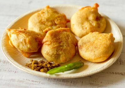Batata Vada - Batata Vada is a popular Indian snack consisting of spiced mashed potato balls coated in chickpea flour batter and deep-fried until crispy and golden, offering a delightful combination of flavors and textures.